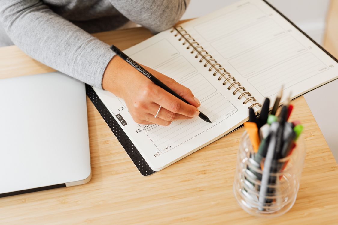 Hand writing a plan beside a laptop