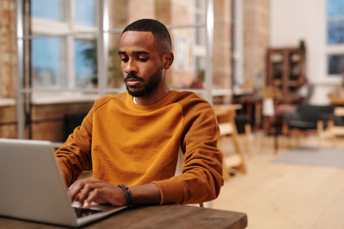 Man focused on his laptop at a sunlit work table